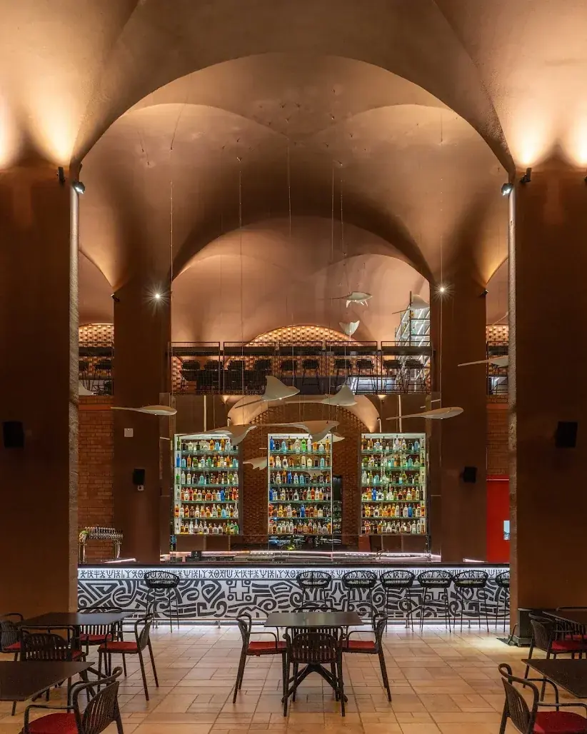 The main hall bar under high brick vaults, with backlit bottle shelves and the pictogram band along the bar front