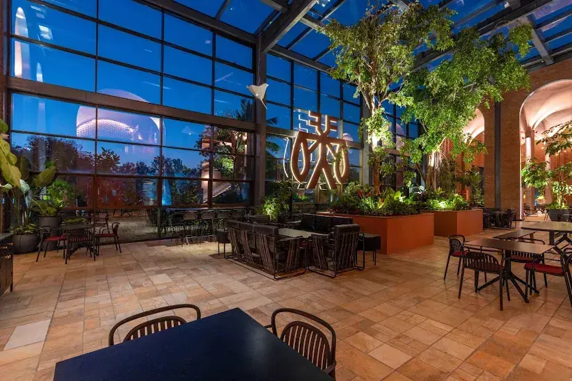 Vari as a large corten steel sculpture on the glasshouse wall at ICB, lit at blue hour above the planted seating
