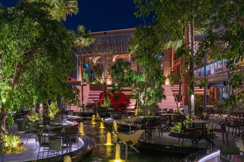 The night courtyard at ICB: lit fountains in a dark water channel, palms overhead and red seating on the steps behind